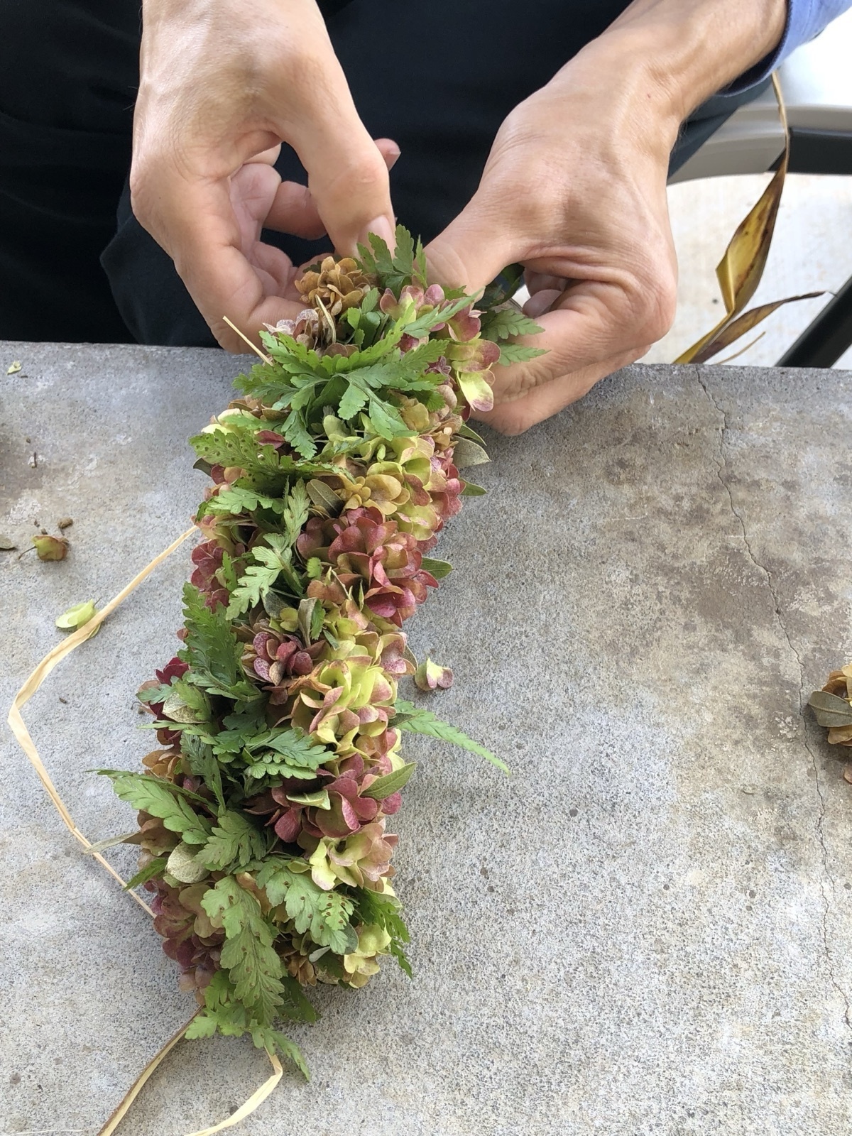 Hands carefully weaving local flowers and foliage into a lei